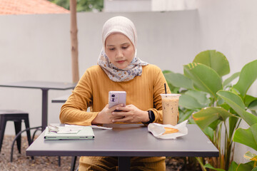 An Asian Muslim woman replying or typing a message on her smartphone at an outdoor cafe