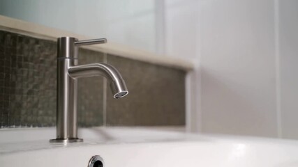 Close-up of a leaking chrome bathroom faucet dripping water slowly into a white sink, highlighting plumbing maintenance and water conservation issues - Powered by Adobe
