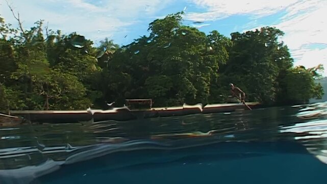 A peaceful journey unfolds as a person paddles along a serene body of water in Papua New Guinea. The clear turquoise waters reflect the lush green islands under a cloudy blue sky.