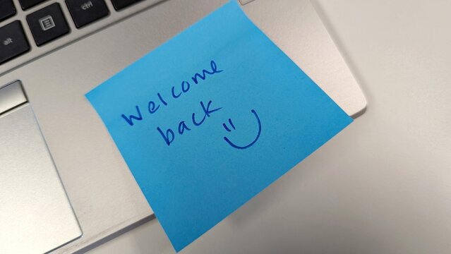 Friend writes a welcome back message with a happy face on blue sticker and leaves on laptop computer