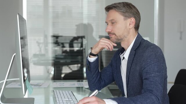 Businessman in a blue jacket thinking and brainstorming ideas while working on computer and taking notes in modern office. Business people concept