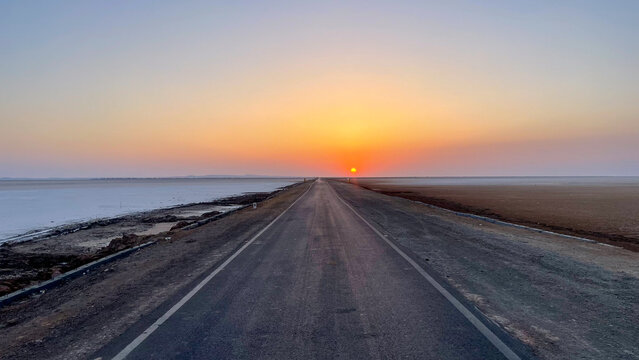 Endless road cutting through the white desert of Rann of Kutch, glowing under a surreal sunrise&mdash;capturing the feeling of driving straight into the horizon.