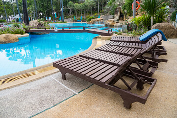 Row of empty wooden lounge chairs beside a swimming pool at a tropical resort with a relaxed outdoor setting