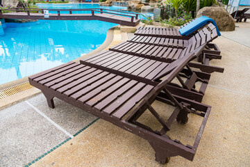 Row of empty wooden lounge chairs beside a swimming pool at a tropical resort with a relaxed outdoor setting