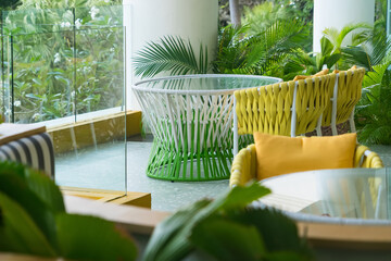Modern outdoor seating area with colorful woven chairs and lush green tropical plants in a relaxing garden setting