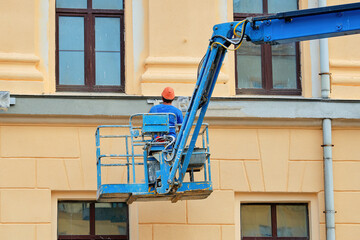 Worker plastering building, plastering job underway on historic building facade with worker on...