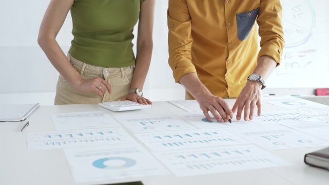 Business professionals analyzing financial reports, pointing at charts during collaborative meeting, discussing data with focused professional demeanor