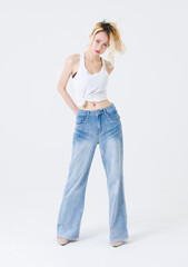Fototapeta premium Asian confident beautiful young woman blonde hair high tied stand wear sleeveless top blue jeans on white background, studio portrait fashion street outfit trendy style pose look at camera full length