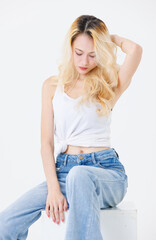 Asian confident beautiful attractive woman blonde long hair sit on cube box wear sleeveless top jeans on white background studio, portrait lifestyle fashion street outfit trendy style look at camera.