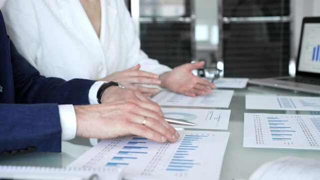 Business people hands discussing financial data and analyzing growth charts on a laptop screen during a corporate meeting with paper documents, showing teamwork and strategy planning