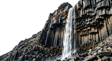 A majestic waterfall cascades down a dramatic cliff face composed of unique hexagonal basalt columns, with bright sunlight creating strong highlights and deep shadows