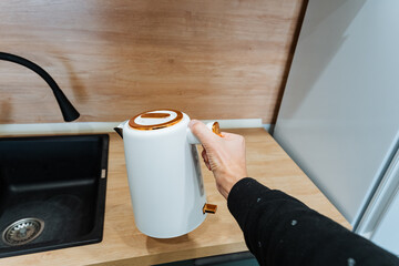 hand pouring hot water from kettle, steam rising above ceramic mug on countertop, careful grip on handle, warm beverage preparation, minimalist kitchen surface, breakfast beverage detail