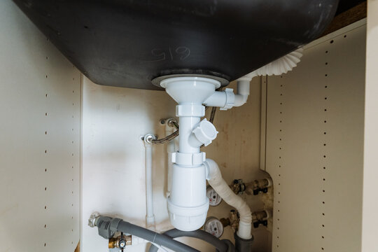 exposed sink plumbing and ptrap, view inside cabinet showing pvc fittings, trap assembly and drain connections, technical maintenance scene for leak checks and diy plumbing diagnostics