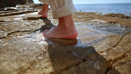 A barefoot person walks on wet rocks by the sea, evoking mindfulness and a connection with nature. The scene suggests a moment of reflection and escape, promoting mental wellbeing and tranquility.