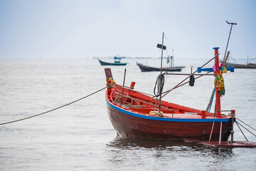 Traditional red fishing boat floating on calm sea with several other boats in the distance on a cloudy day