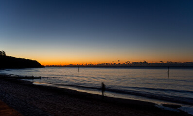 A solitary man walks along a beach at sunrise. Subtle motion blur. Solitude and relaxation. Coastal walk. Mental health image.
