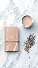 A minimalist composition featuring a marble-patterned notebook, a cup of coffee, and a dried plant stem arranged on a marble surface.