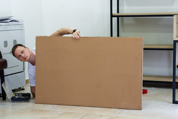Man cautiously looking over large cardboard panel