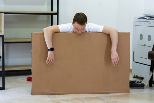 Bored man slouching with arms over cardboard panel indoors