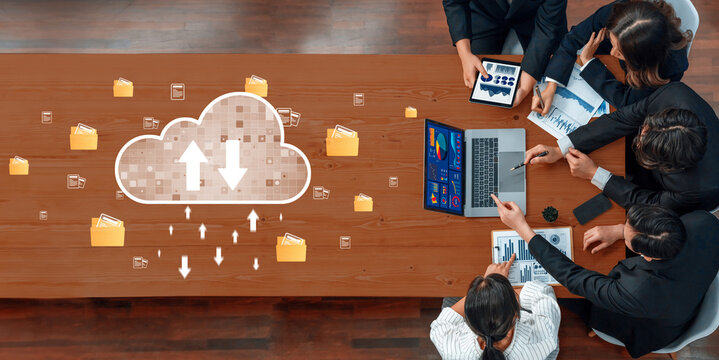 A diverse business team collaborates around a table with digital devices, focused on cloud data transfer while analyzing charts and information for strategic growth. Trope - Powered by Adobe