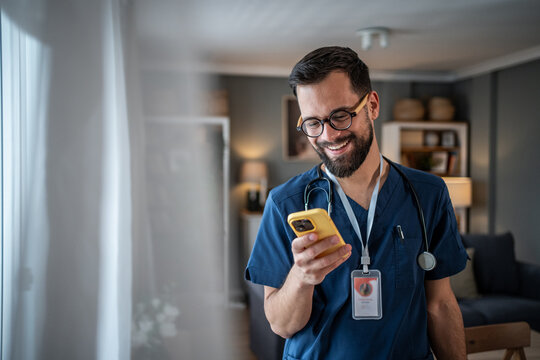 Male doctor in scrubs using smartphone smiling - Powered by Adobe