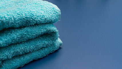 A close-up of two fluffy, folded teal or turquoise towels stacked neatly on a dark navy blue surface, emphasizing texture.