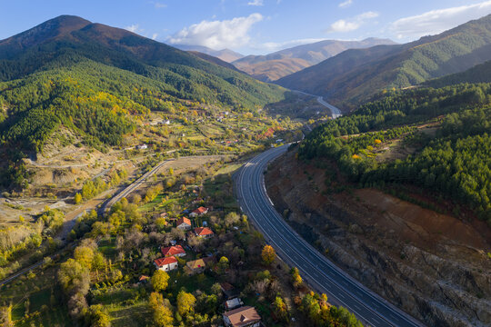 Aerial view of the A1 motorway winding through the mountain valleys of Mirdita, surrounded by autumn forests and scattered hillside homes.