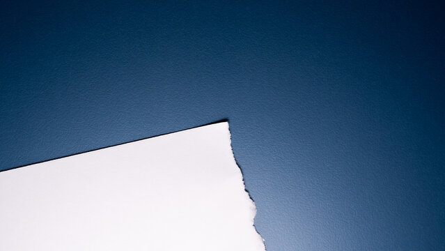 A white sheet of paper with a clean corner and one roughly torn edge rests on a smooth, deep navy blue background.