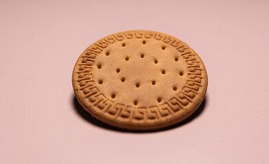 A single round, golden-brown biscuit with a decorative edge and docking holes rests on a clean, light pastel pink background.
