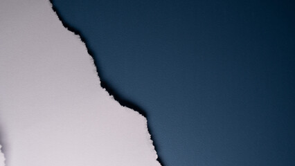 A close-up of a torn white paper edge creates a rough, textured border against a smooth, deep blue background, symbolizing change or contrast.