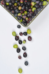 An overhead vertical shot shows a glass dish of mixed olives in the top corner with some olives spilled below onto a white background