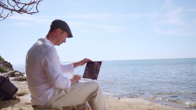 A focused digital nomad works on a laptop by the serene sea, embodying remote work freedom. The clear sky and tranquil waters highlight a peaceful, productive environment.