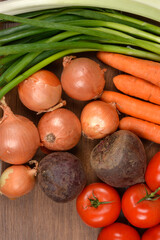 A vertical, top-down image featuring a collection of fresh, colorful vegetables including onions, carrots, beets, tomatoes, and spring onions, on a wooden background