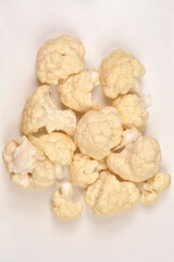 A close-up, overhead shot features a cluster of white cauliflower florets piled together on a plain white surface