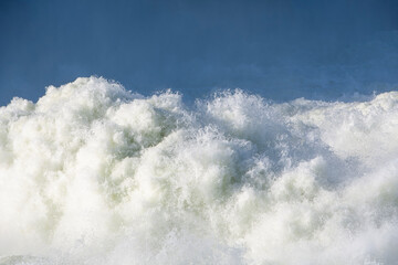 Strong powerful stream of rushing river water flows fast creating white foam and splashes against the deep blue background for a beautiful abstract natural texture of liquid energy outdoors