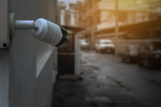 Old security camera mounted on the wall and monitoring at some cars parking on side road with sunset and lowlight vision. Selective focus and copy space.