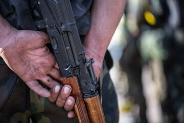 Close up rear view of dirty male soldier hands holding a vintage Kalashnikov assault rifle weapon...