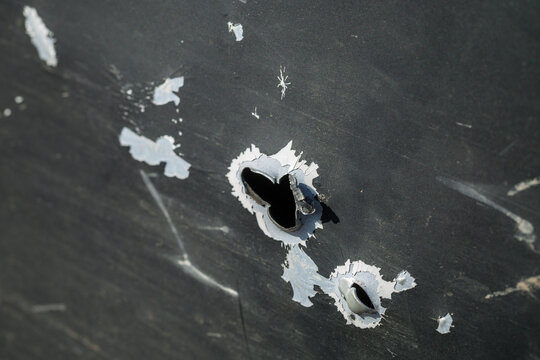 Close up detail view of a jagged shrapnel hole in the dirty scratched green metal door of a mil vehicle damaged by heavy artillery or mortar shelling during dangerous war combat action on the street