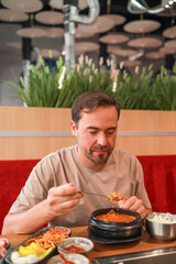 A man enjoys traditional Korean kimchi jjigae soup at a Korean restaurant. Asian food