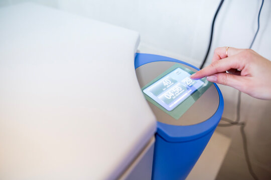 Close up view of a scientist hand pressing the touchscreen control panel of a modern electronic laboratory centrifuge device setting the timer and speed for sample preparation process