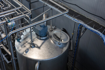 The interior of a modern industrial plant, such as a food, beverage, or chemical factory. Large stainless steel tanks are connected by a complex system of pipes, valves, and sensors.