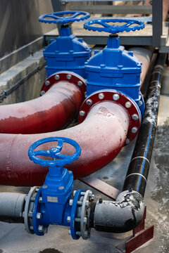 Large red industrial pipes, covered in thick white dust, are connected to large blue gate valves. This heavy-duty plumbing system with flanges and bolts is part of a fluid line in a factory.