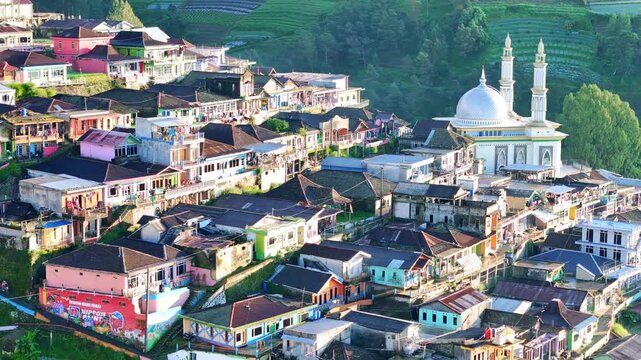 Aerial view of a picturesque Indonesian highland village with colorful houses, a mosque, and terraced fields on a sunny day. Nepal Van Java, Mount Sumbing.