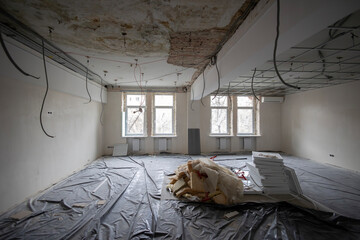 The interior of a room during renovation. The floor is covered with black plastic, and the ceiling...