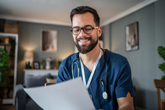 Male nurse or doctor smiling and reading documents at home