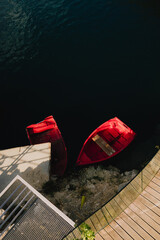 Fototapeta premium Two vibrant red boats sit near modern dock with wooden planks and concrete sections, creating striking contrast against dark, still water. Bright red boats mooring alongside sleek wooden concrete dock