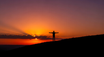Embracing the Sunrise Silhouette: A lone figure stands poised against the canvas of a vibrant sunrise, arms outstretched, embodying freedom and hope. 