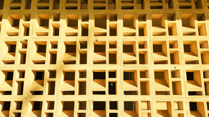 Modern yellow concrete roster wall texture. The repeating geometric pattern creates unique shadows under the bright sunlight