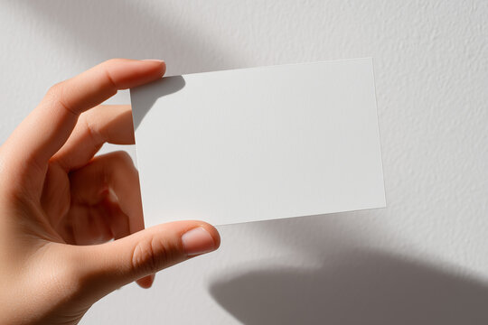 Minimal white business card mockup held by hand — clean textured paper with studio lighting and copyspace for branding or corporate identity designs