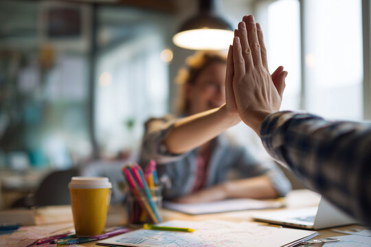Creative team high-five in a bright coworking studio celebrating collaboration and successful brainstorming over sketches, coffee, and colorful supplies